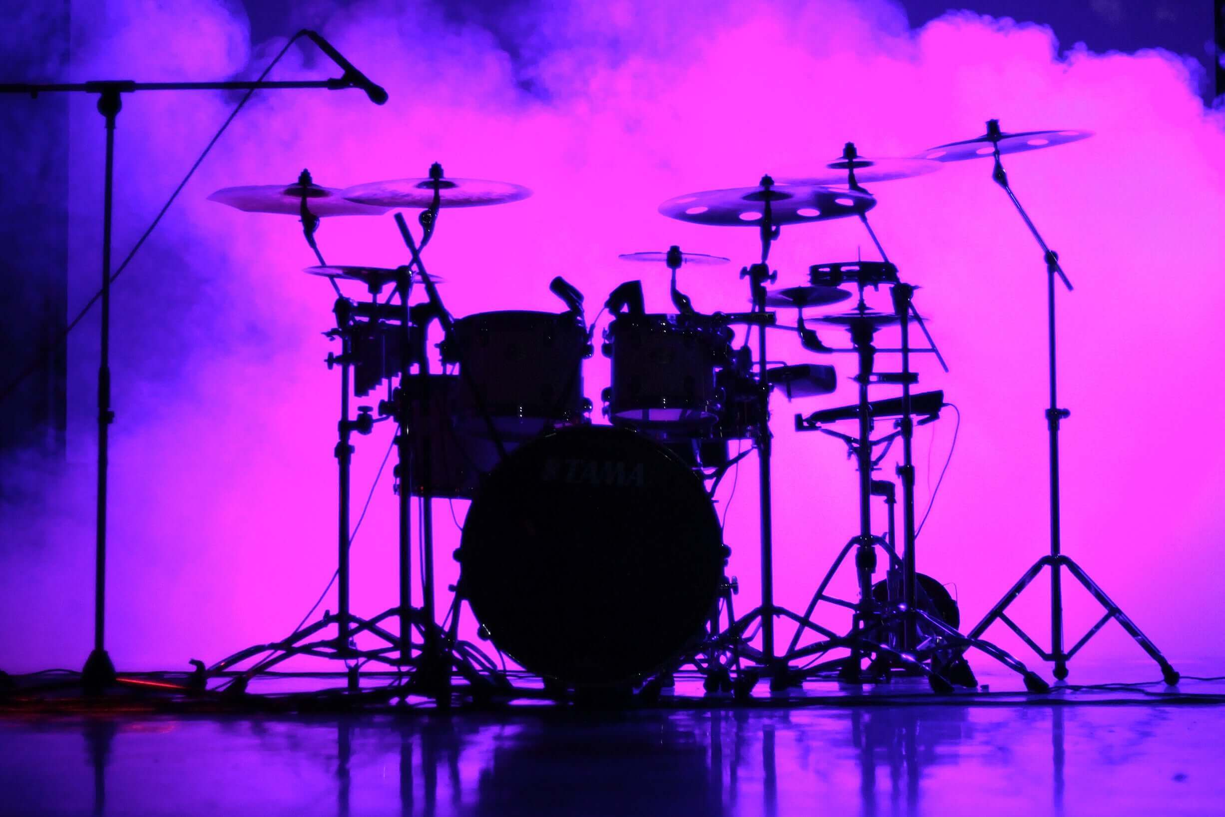 Drum set illuminated by purple smoke, creating a dramatic atmosphere for music performance.